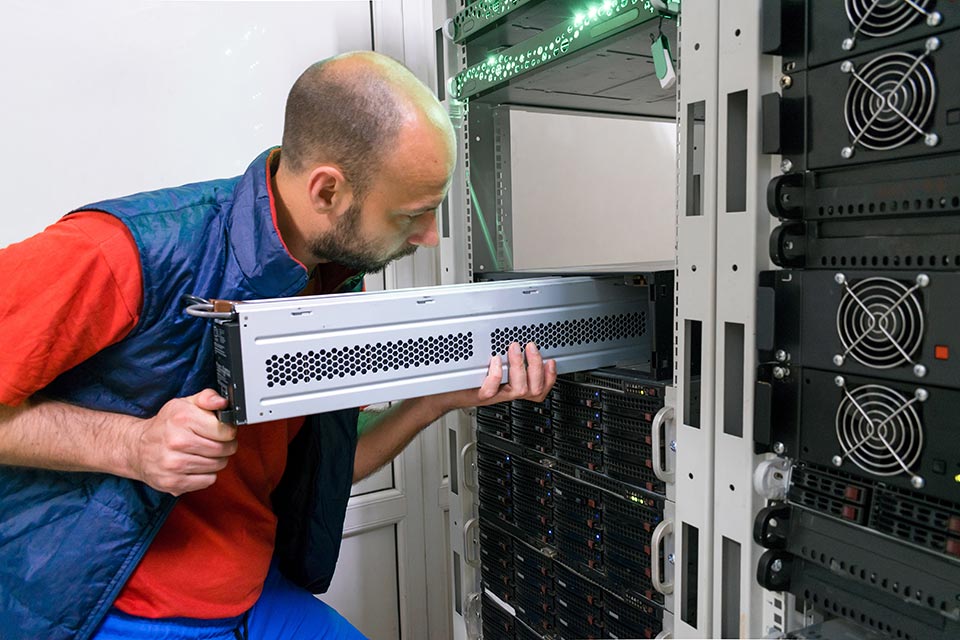 The man installs a new battery into the uninterruptible power supply. Replacing the power module in the server room rack.
